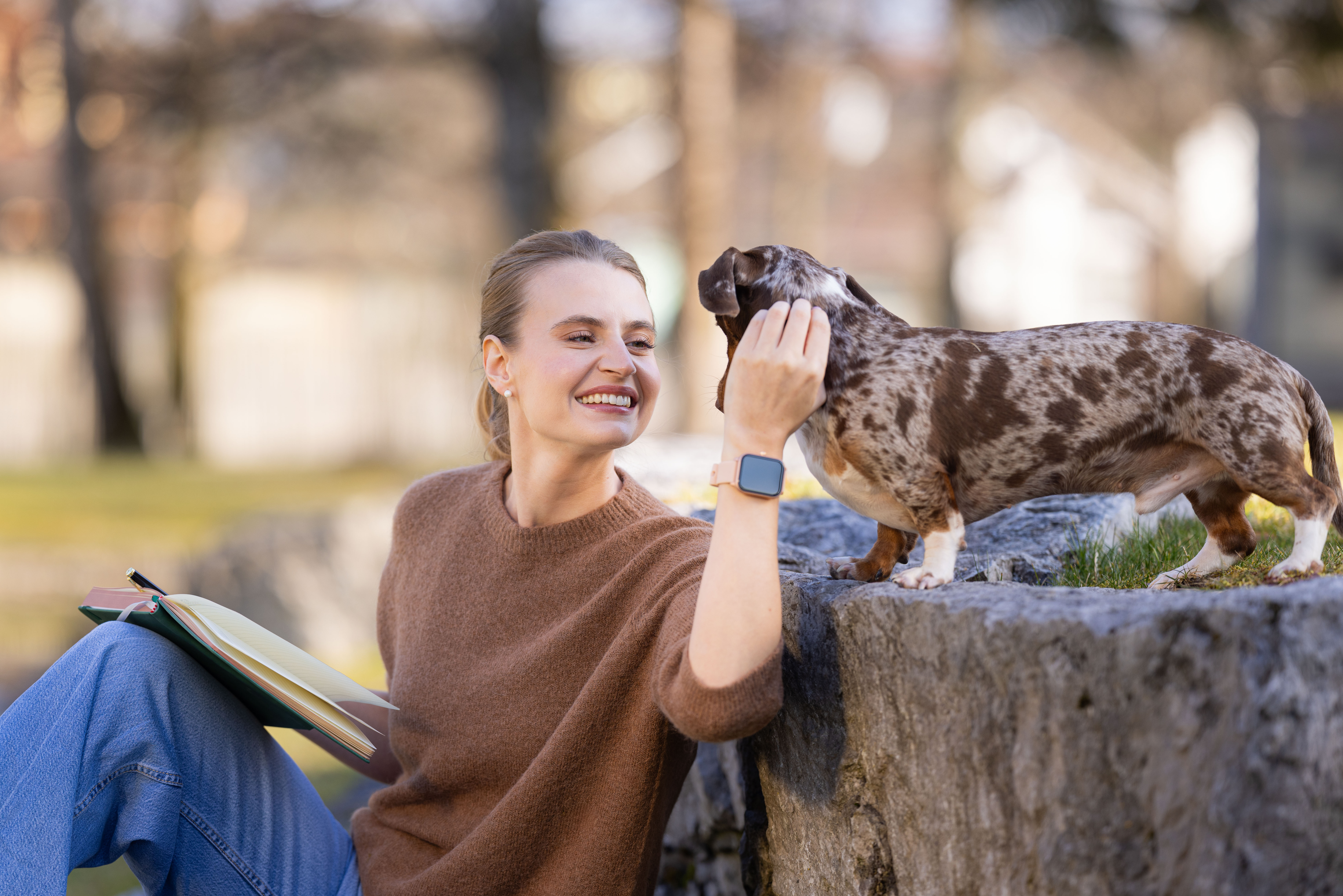 Frau streichelt Hund im Freien, sie hält ein Notizbuch.