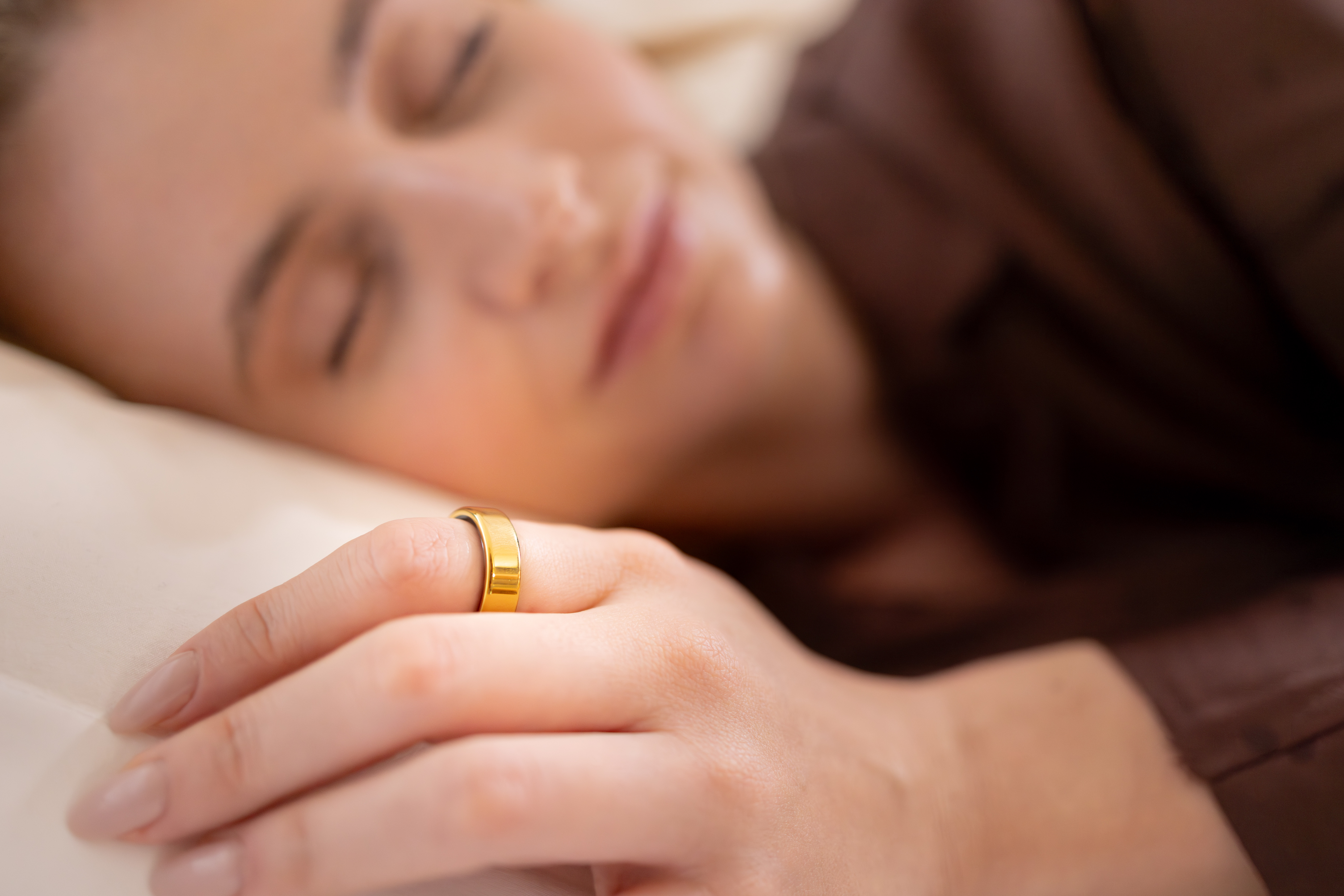 Eine Frau schläft, ihr Finger mit einem goldenen Ring ruht auf einem Kissen.