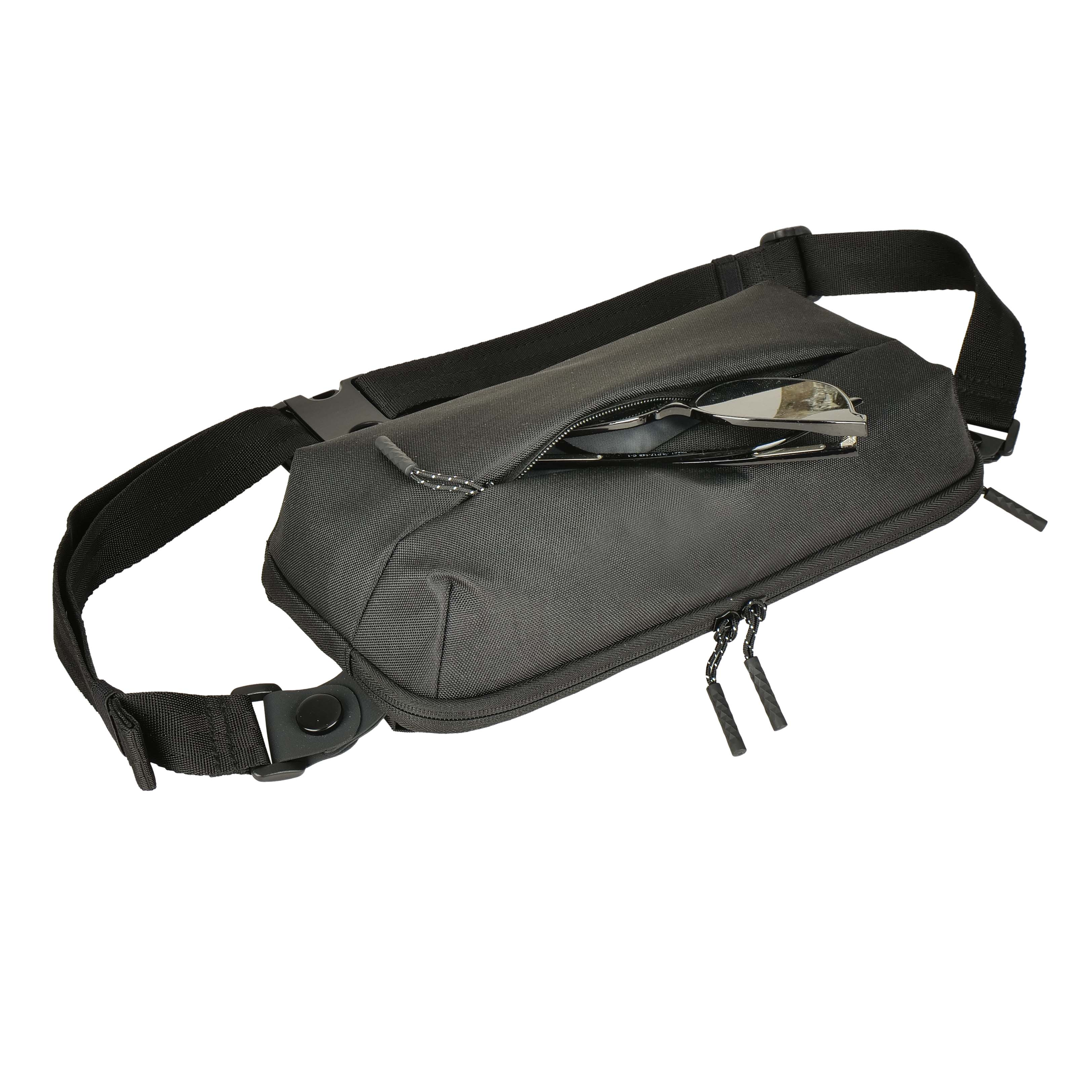 Eine graue Bauchtasche mit Reißverschluss und einer Tasche, in der eine Sonnenbrille liegt.
