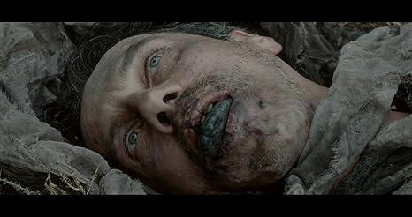 Nahaufnahme des Gesichts eines Mannes mit blauen Augen, dunklem Haar und bedrücktem Ausdruck, der in Trümmern liegt.