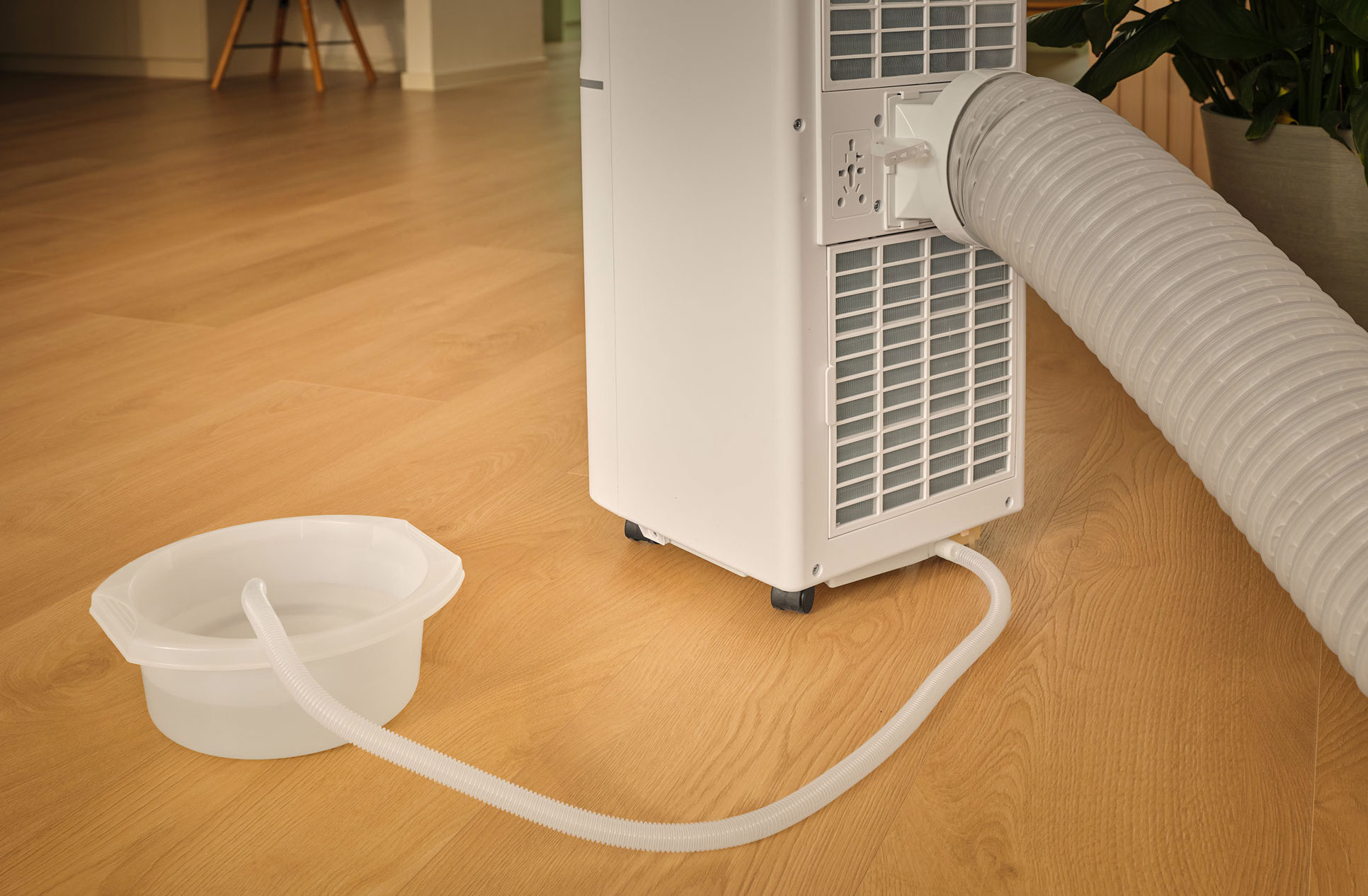 Biały wąż odprowadzający przenośnej klimatyzacji prowadzi do miski z wodą.