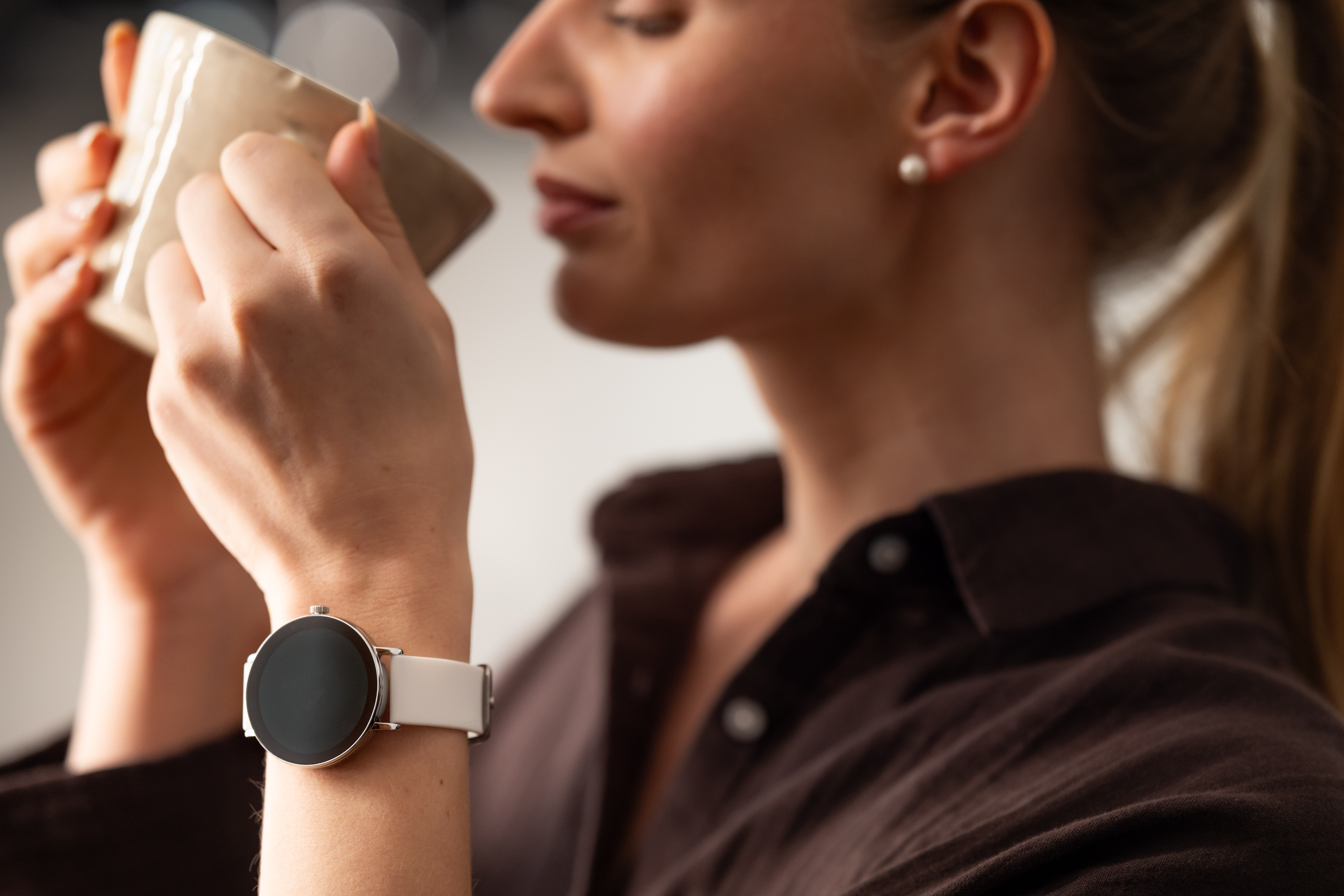 Eine Frau mit einem Smartwatch trinkt aus einer Tasse.