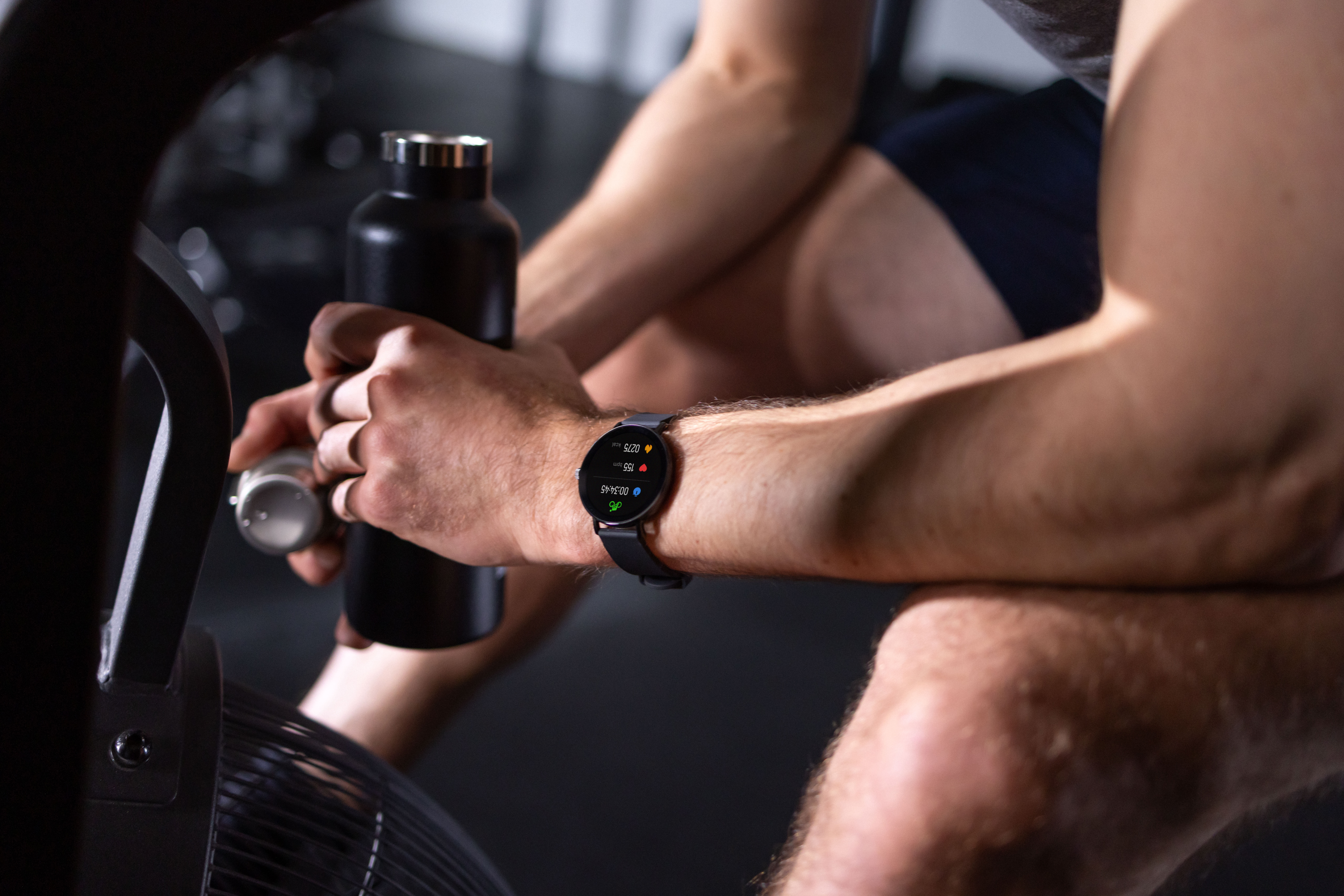 Mann mit Smartwatch hält schwarze Wasserflasche neben Trainingsgerät.