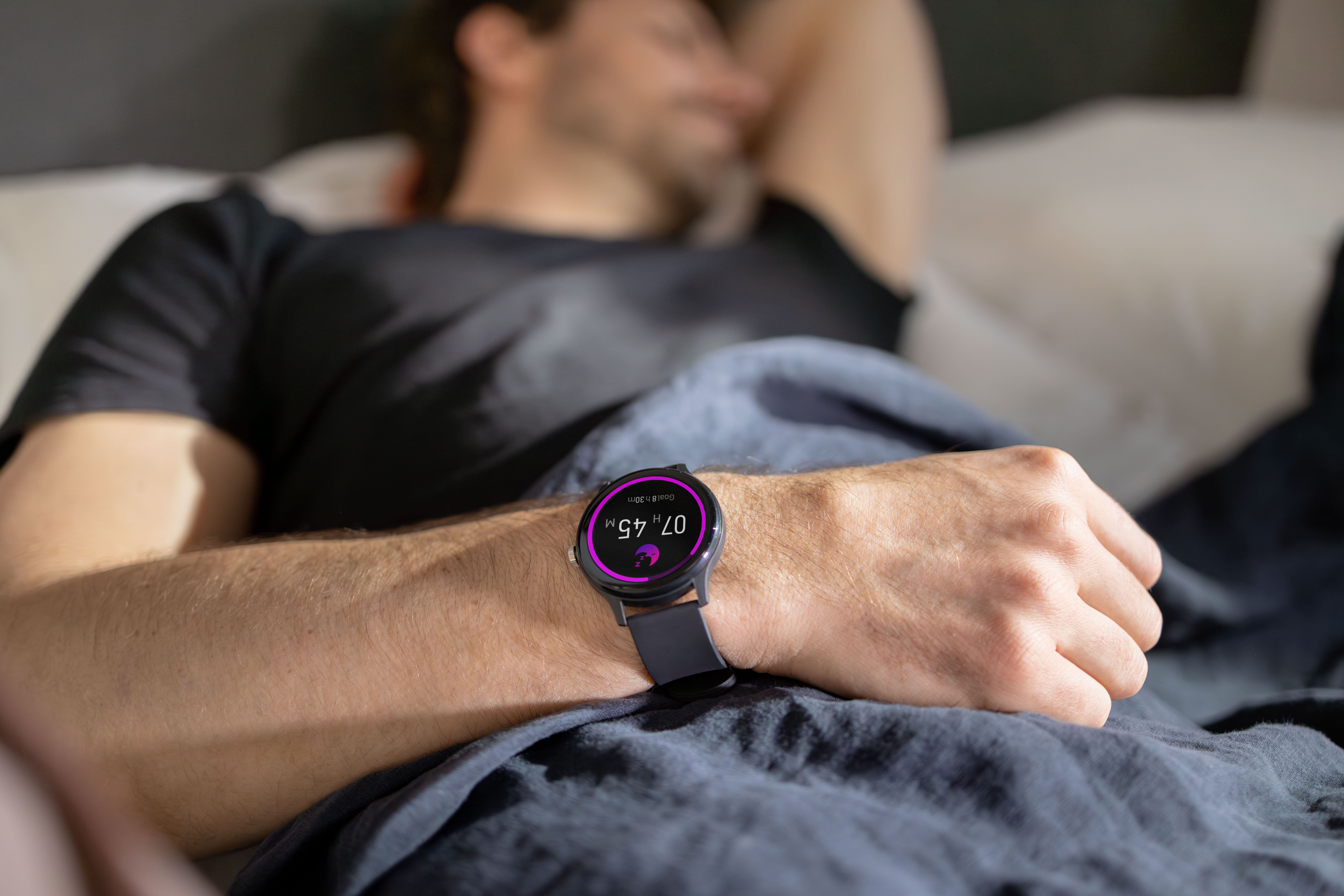 Mann schläft im Bett, trägt eine Smartwatch, die 07h 45m anzeigt.
