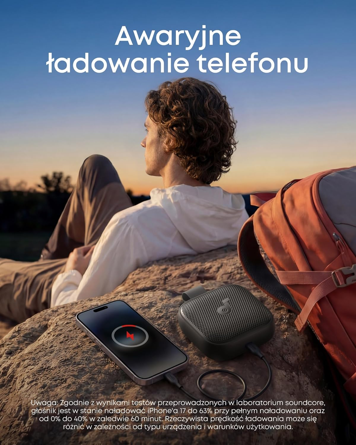 Mężczyzna ładuje telefon powerbankiem na zewnątrz o zachodzie słońca.