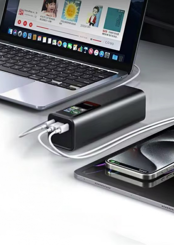 Fekete power bank csatlakoztatva laptophoz és telefonhoz. Táblagép a telefon alatt.
