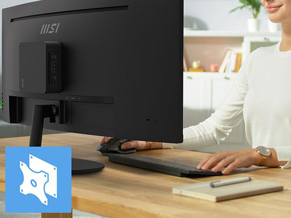 Mini-PC an Monitorrückseite montiert, Frau arbeitet am Schreibtisch.