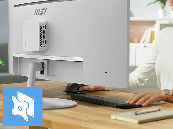 Ein weißer Mini-PC ist an der Rückseite eines weißen Monitors montiert. Eine Person tippt auf einer Tastatur.