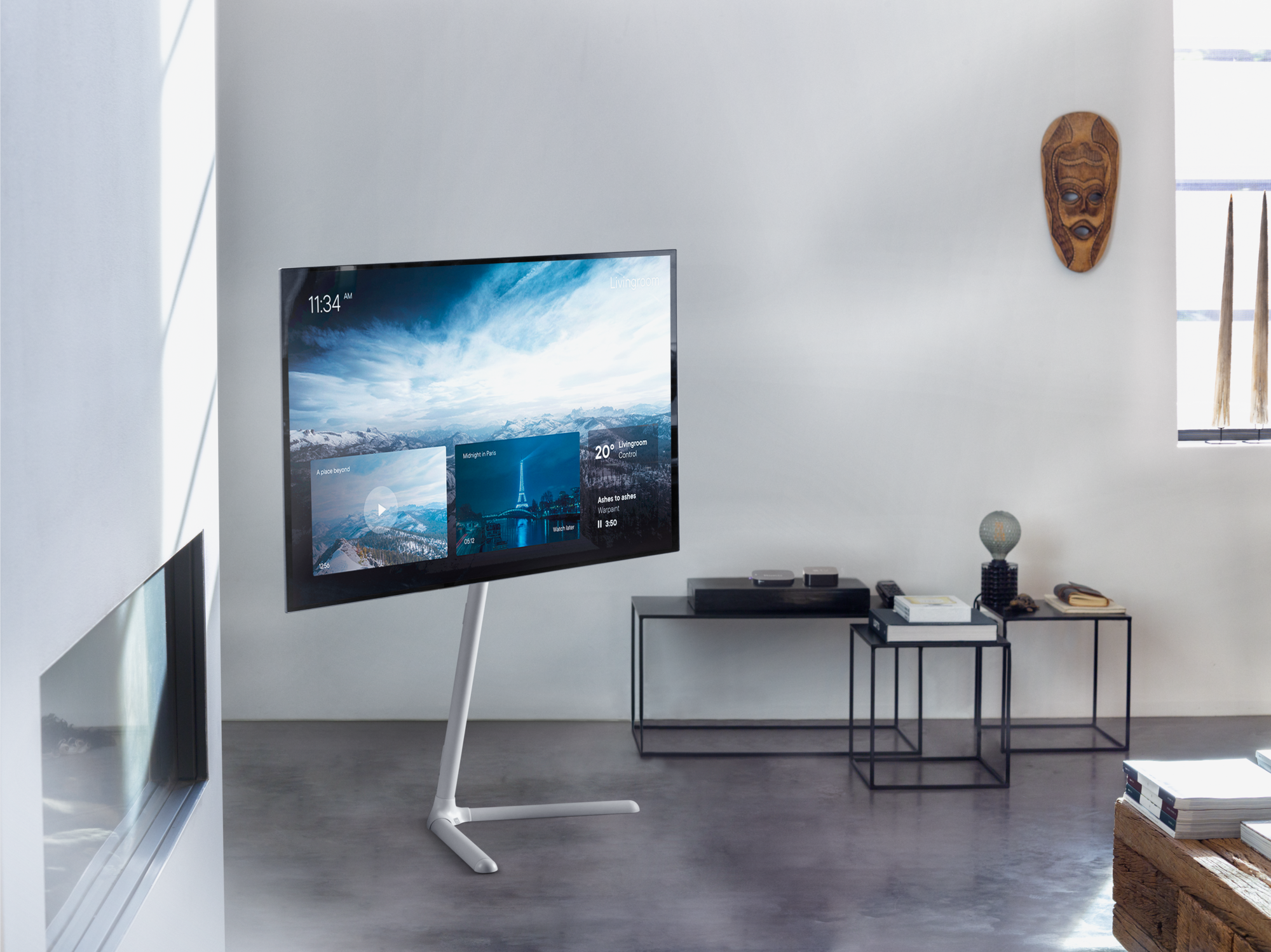 Un televisor moderno sobre un soporte muestra un paisaje. Una máscara cuelga de la pared.