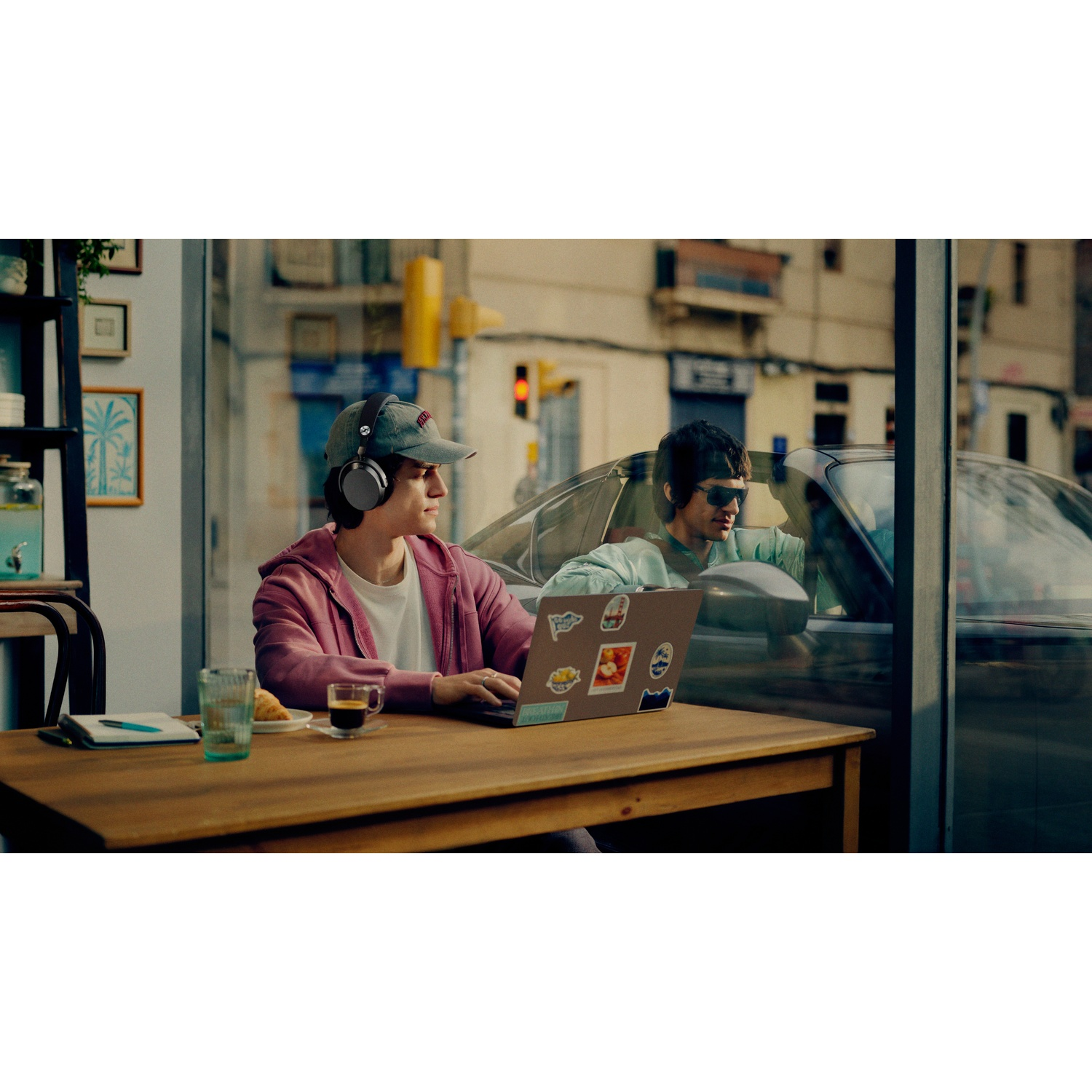 Man with headphones works on laptop in cafe. Man in car outside.