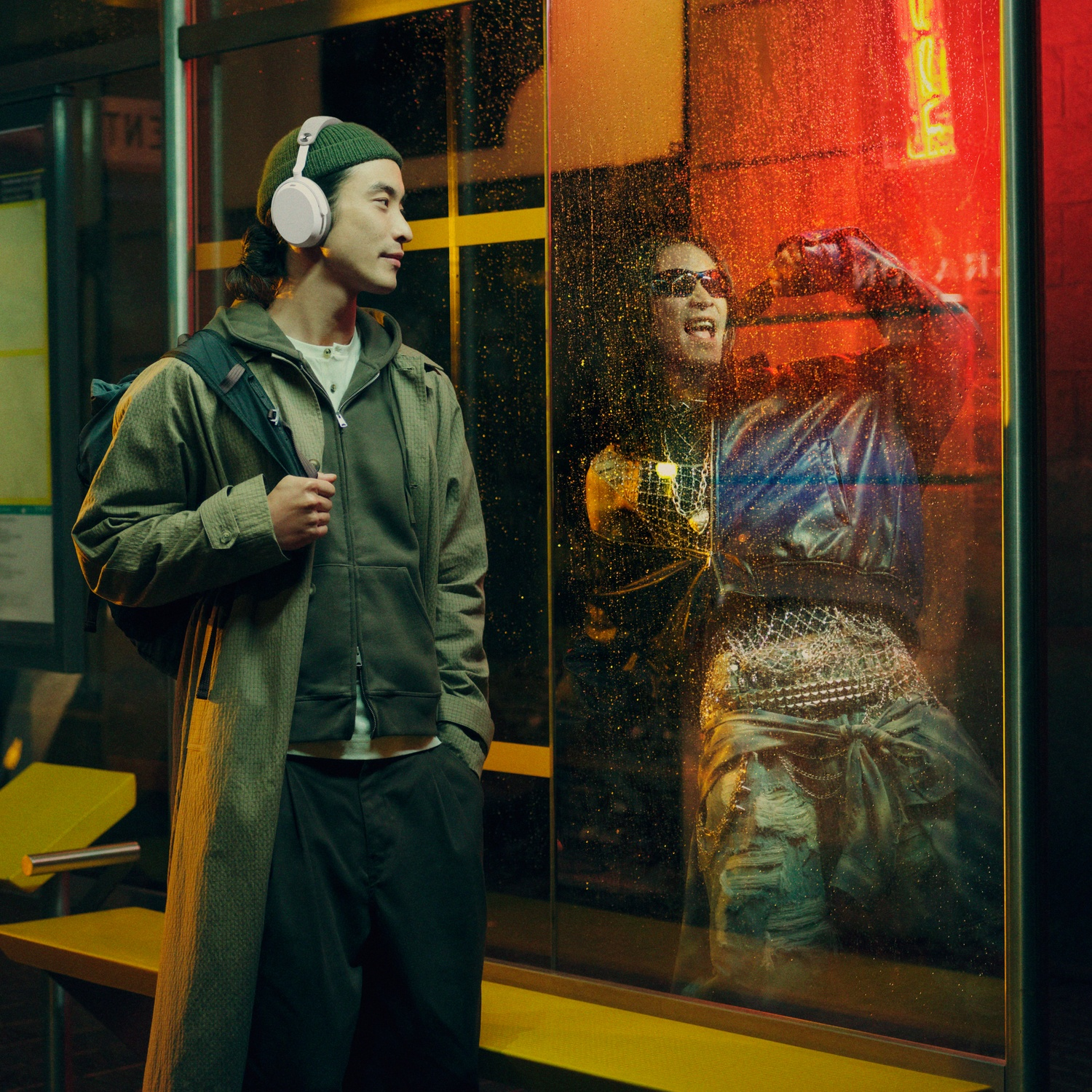 Man with headphones waits in the rain. Reflection of a person wearing sunglasses.