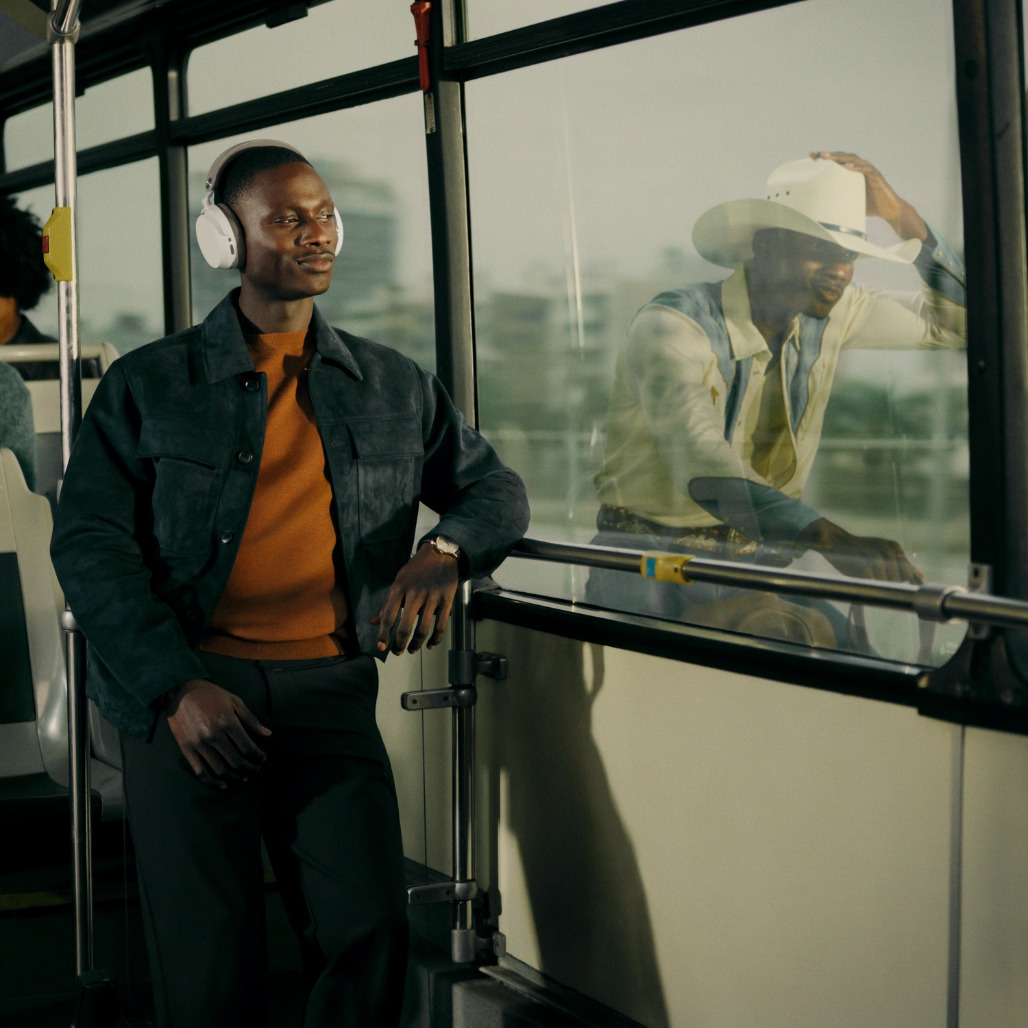Man met koptelefoon in bus, cowboy weerspiegeld in raam.