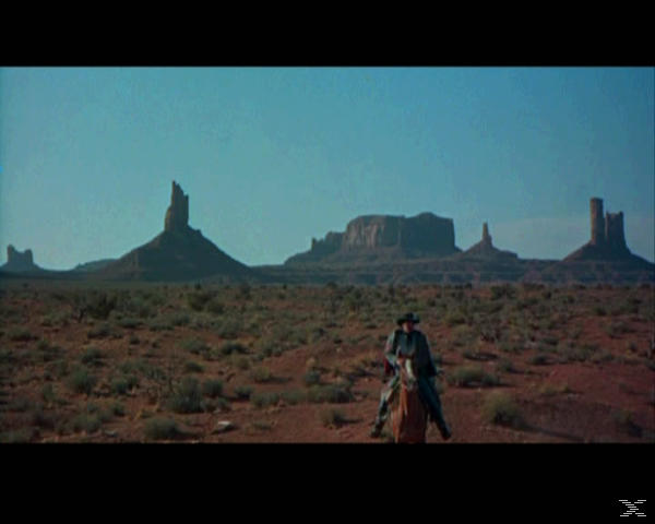 Ein Cowboy reitet auf einem Pferd durch eine Wüstenlandschaft mit Tafelbergen.