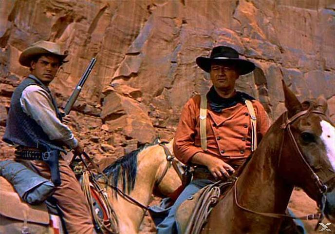 Zwei Cowboys reiten auf Pferden vor einer Felswand, einer hält ein Gewehr.