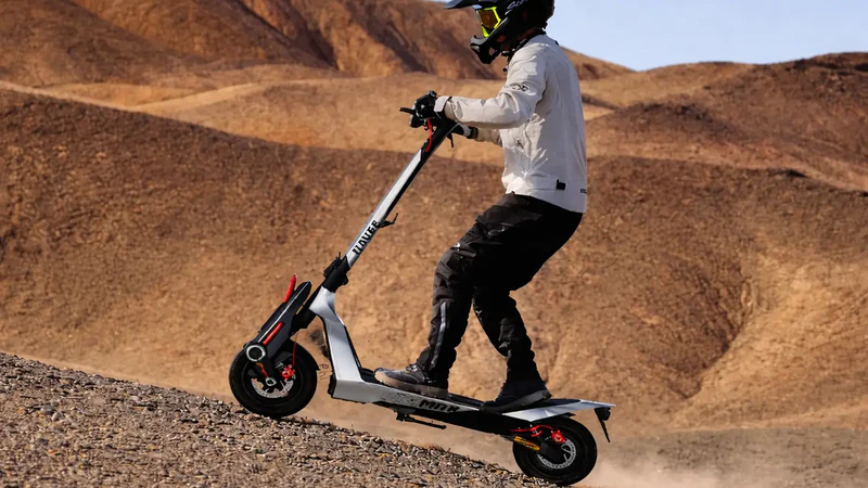 Ein Fahrer auf einem E-Scooter fährt bergauf auf einem staubigen, felsigen Hang.