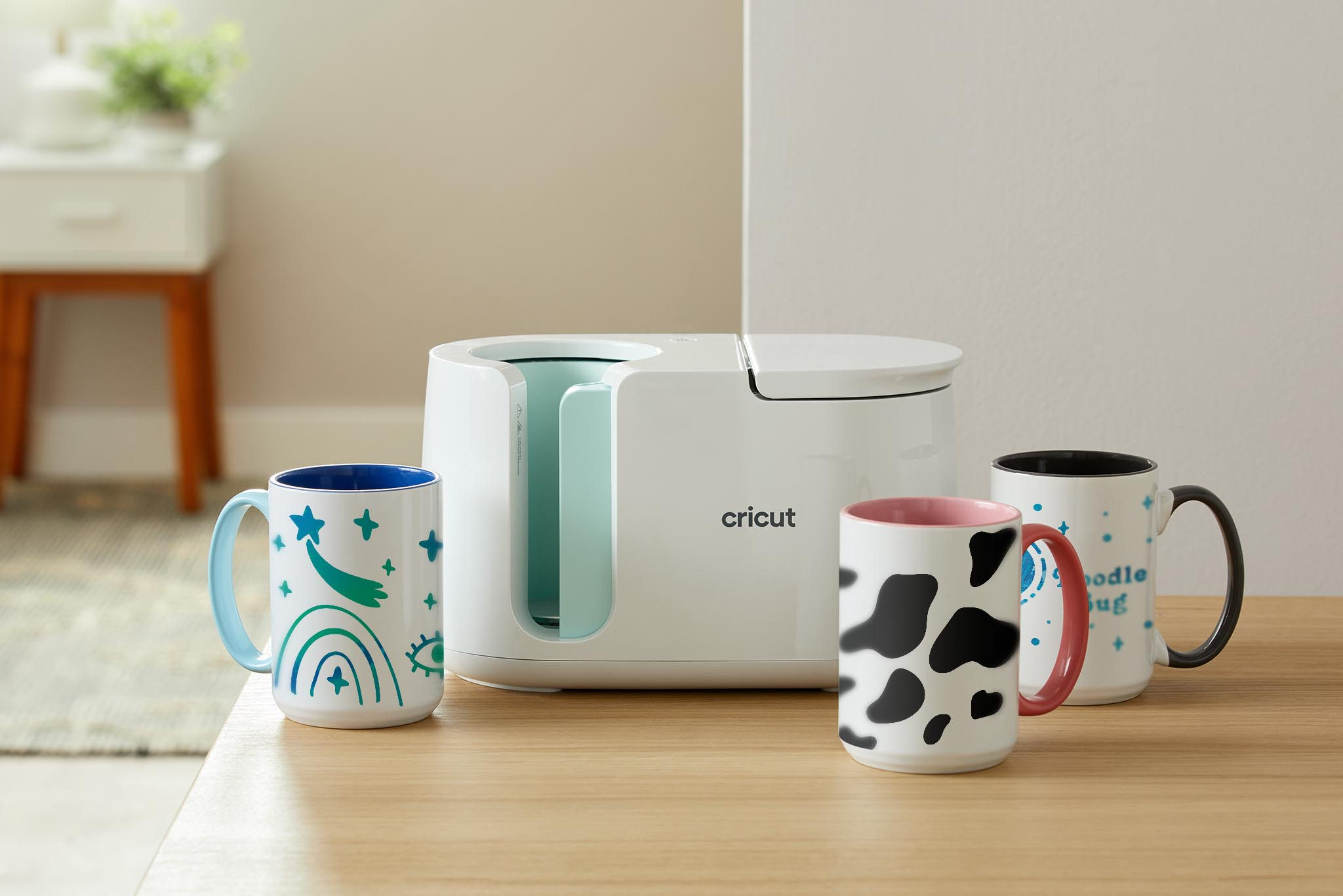 Önünde üç süslü kupa bulunan beyaz bir Cricut kupa presi.