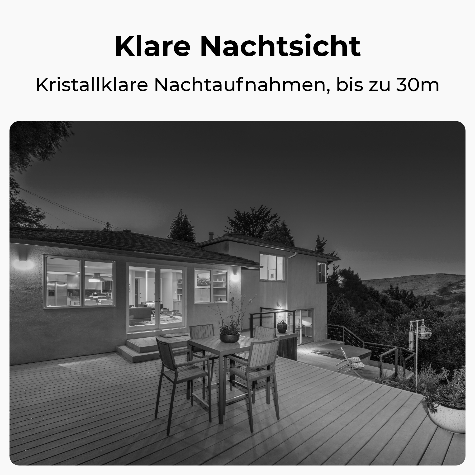 Ein Haus bei Nacht mit einer Terrasse, Stühlen und einem Tisch. Innen brennt Licht.