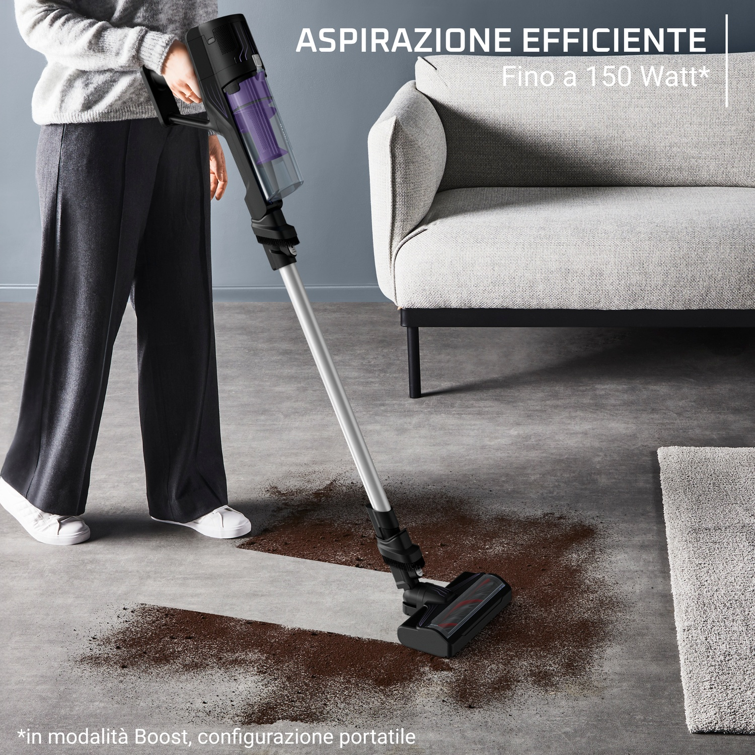Una persona aspira terra con un aspirapolvere nero senza fili su un pavimento in cemento.