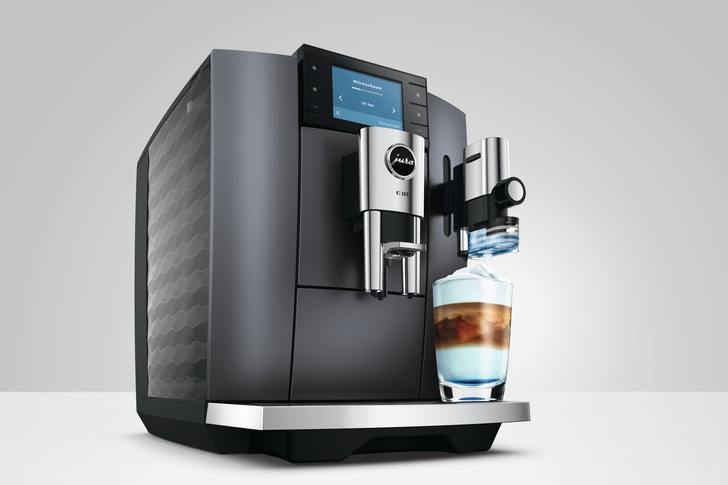 Eine graue Kaffeemaschine bereitet ein Getränk mit Milchschaum zu.
