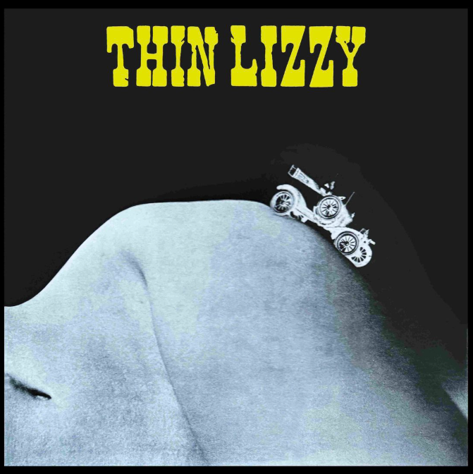 Ein altes Auto fährt über eine gebogene, helle Oberfläche. Oben steht THIN LIZZY.