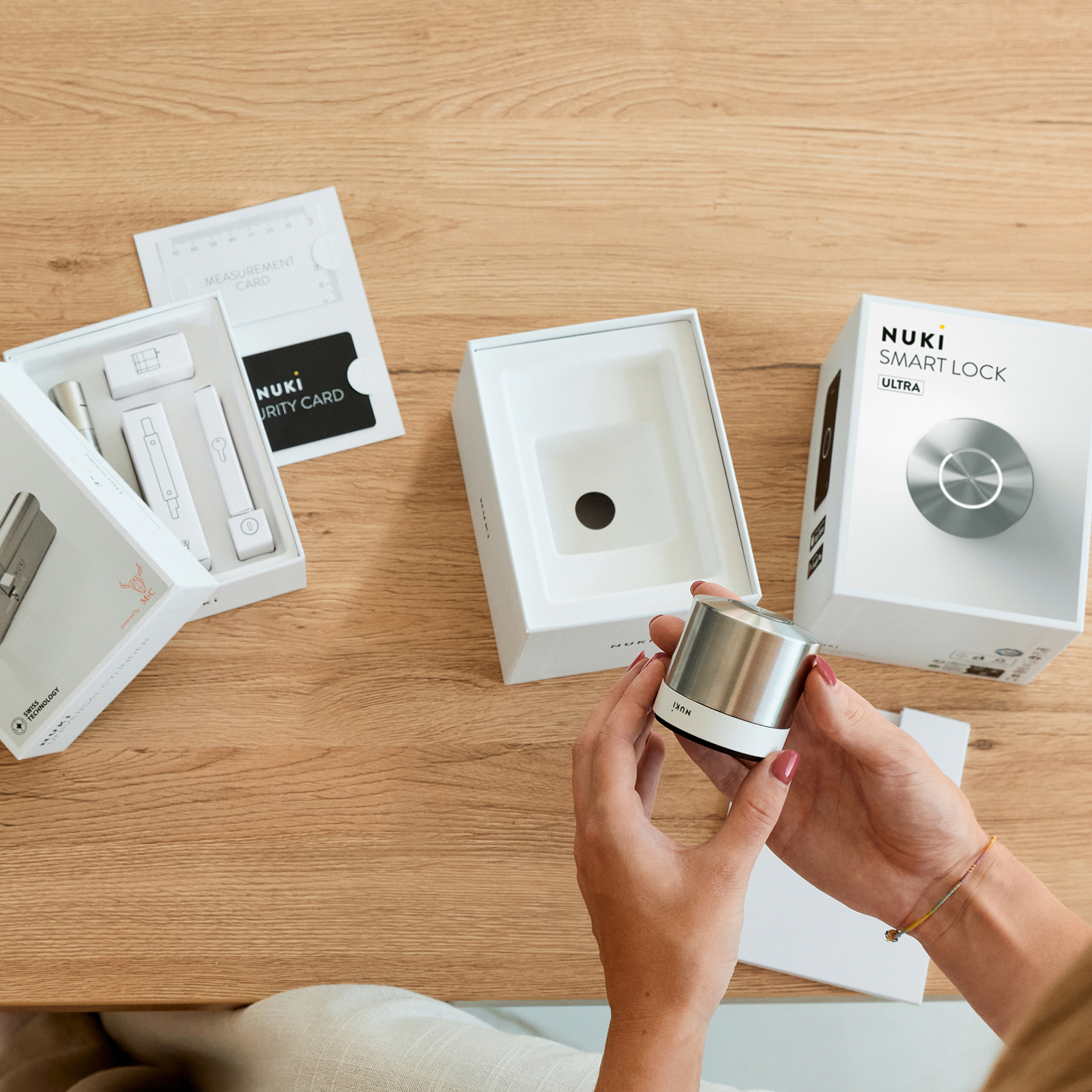 Egy személy Nuki Smart Lock eszközt tart; csomagolás van a közelben.