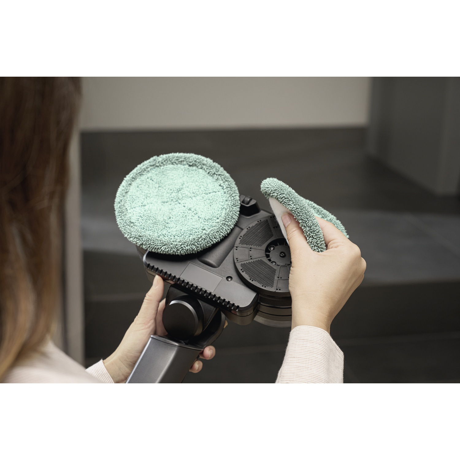 Una persona tiene un pulitore per pavimenti nero con due tamponi di pulizia verdi.