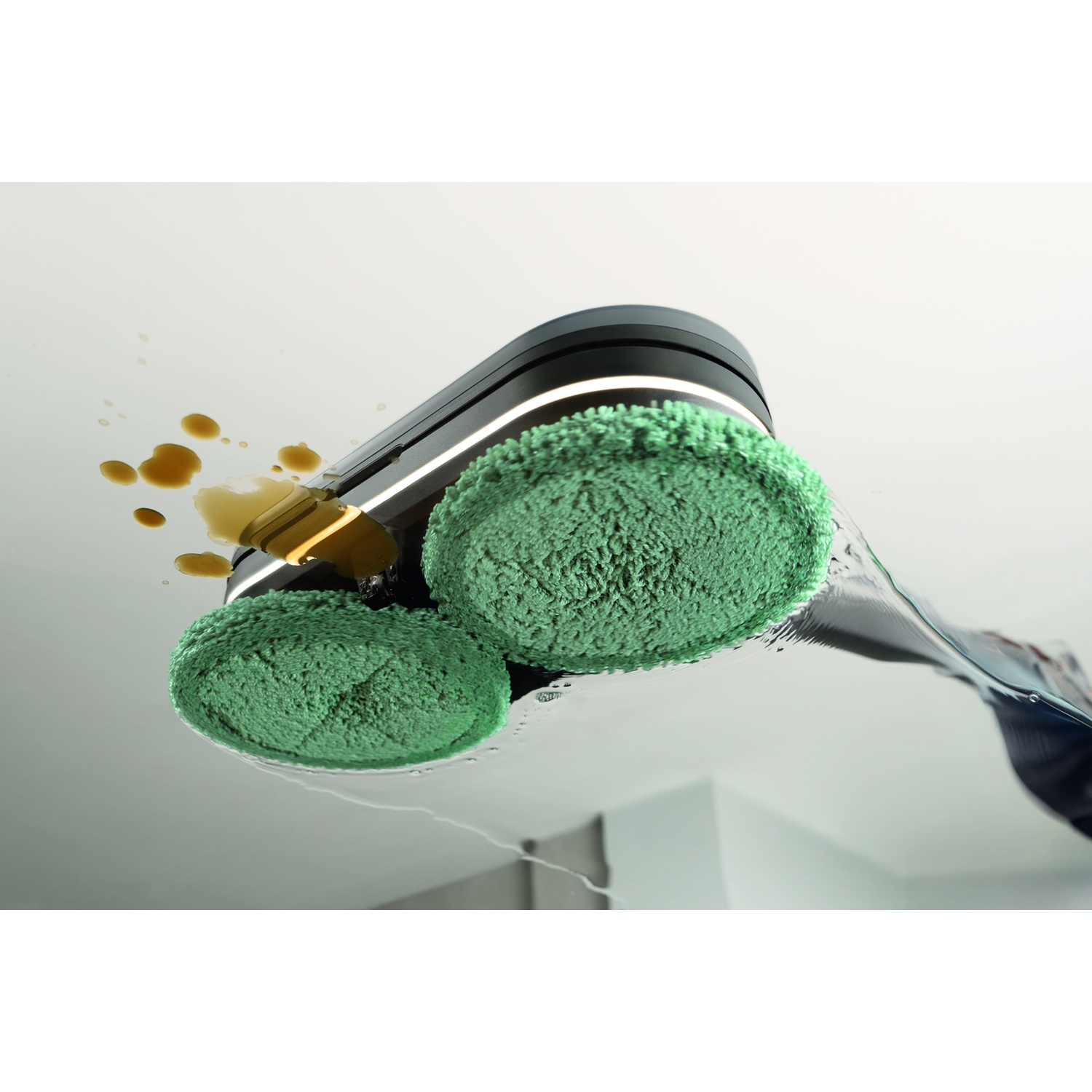 Un robot per pulizie con spazzole verdi pulisce liquido su una superficie bianca.