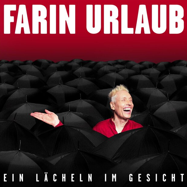 Ein Mann mit blonden Haaren lacht inmitten vieler schwarzer Regenschirme.