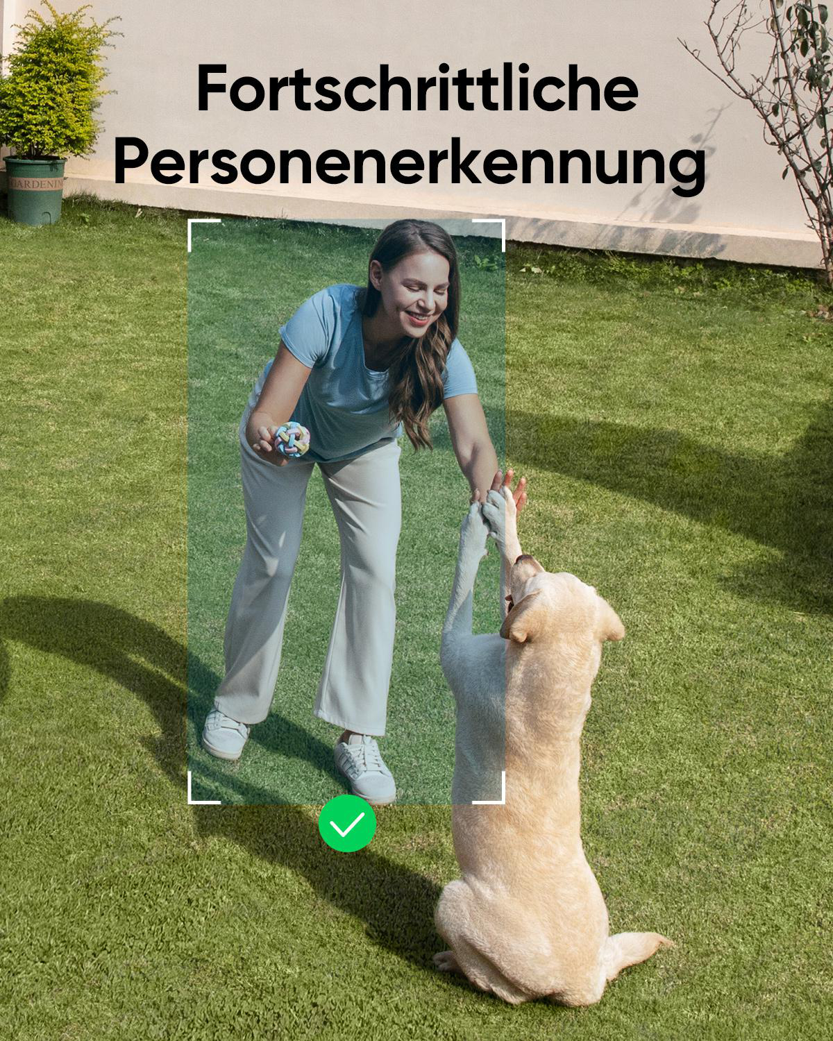 Eine Frau gibt einem Hund im Garten die Pfote, während sie ein Spielzeug hält.