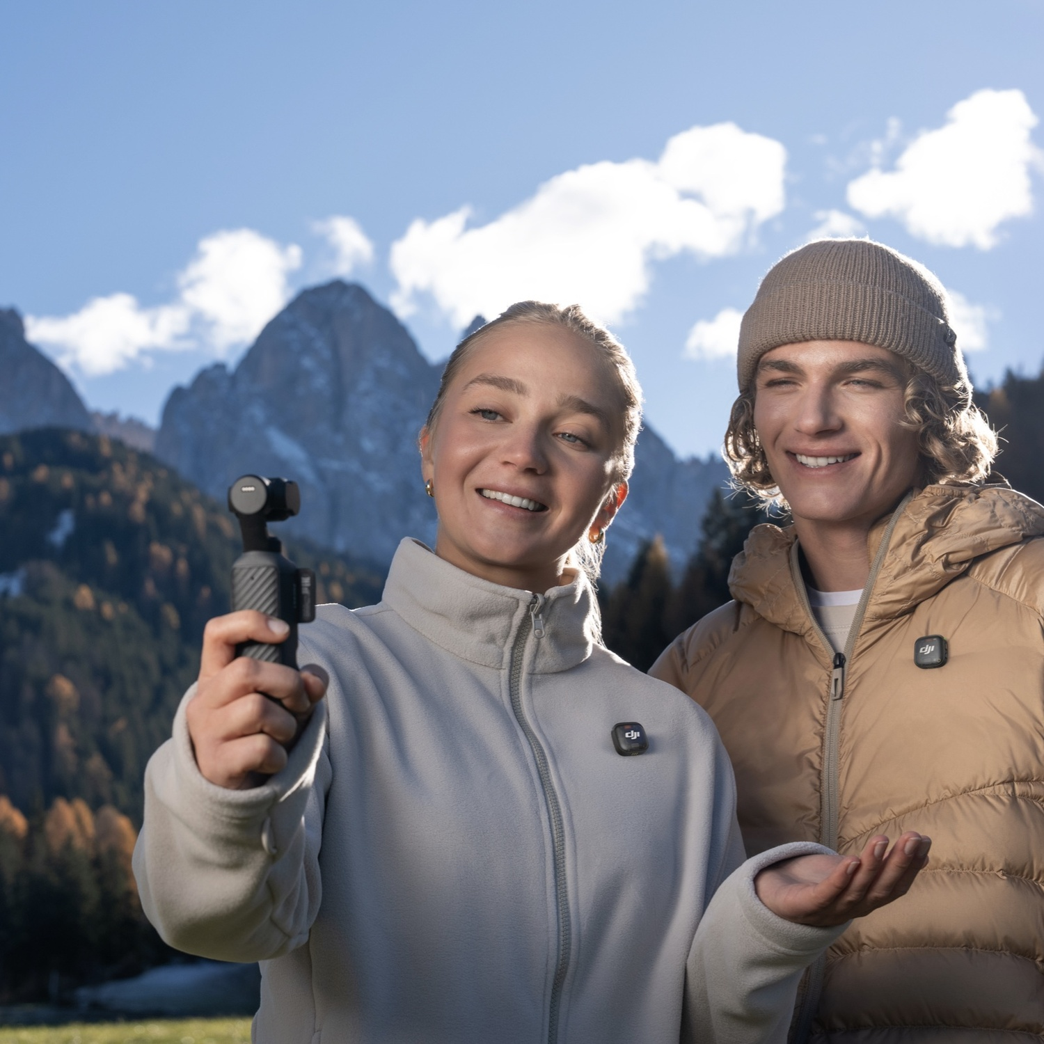Una giovane coppia sorride in montagna, tenendo una telecamera.