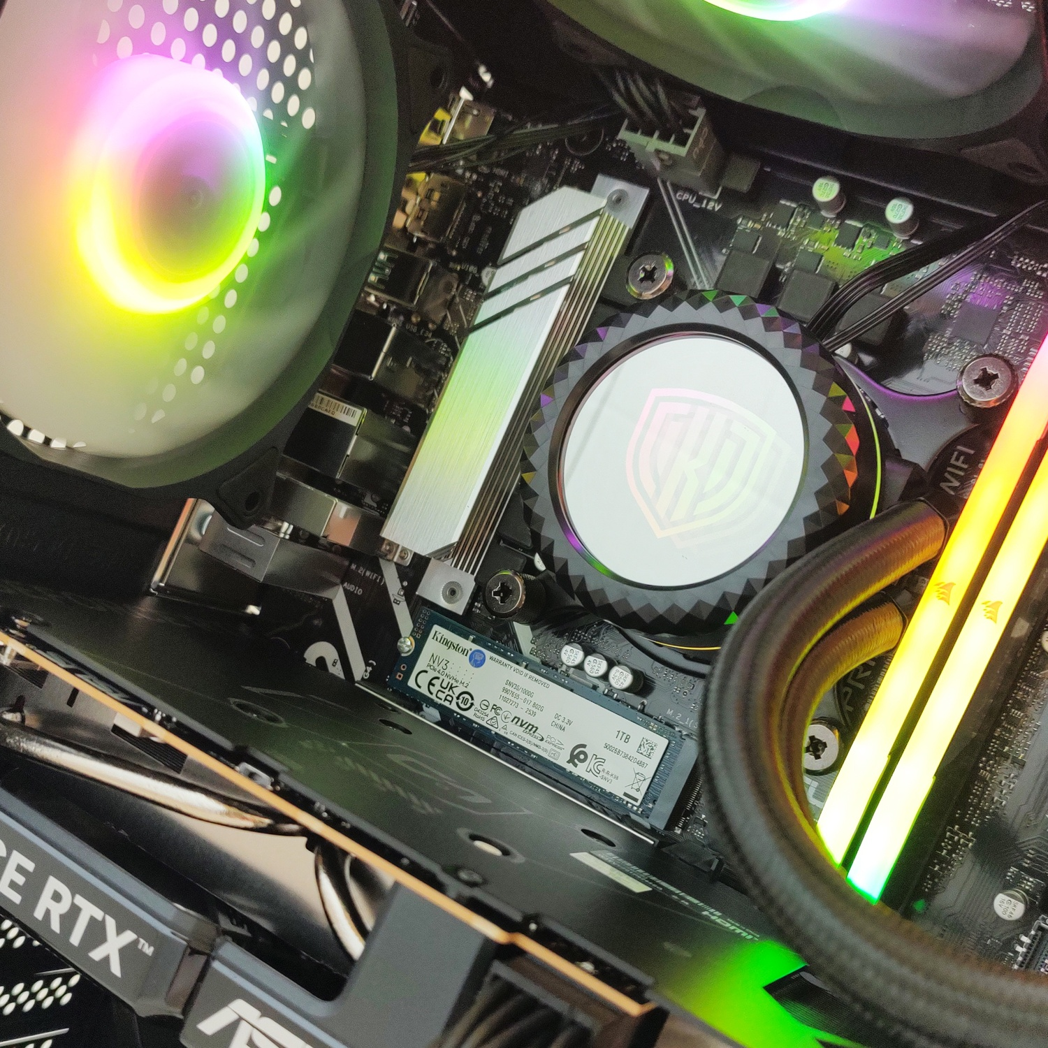 Primo piano di componenti interni di un computer, con ventole RGB, dissipatore CPU, RAM e GPU.