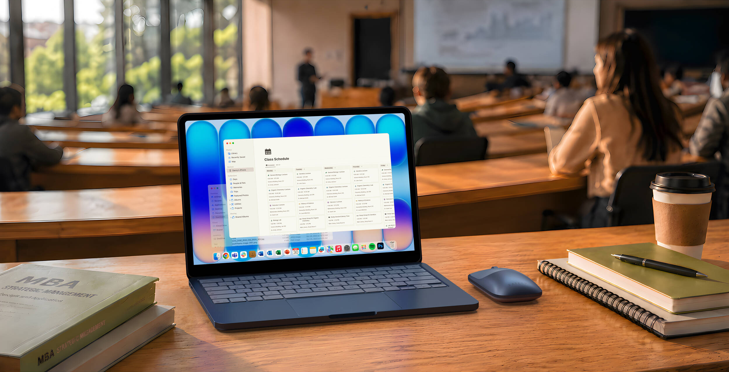 Ordinateur portable ouvert dans une salle de classe affichant un emploi du temps. Livres et café sur le bureau.