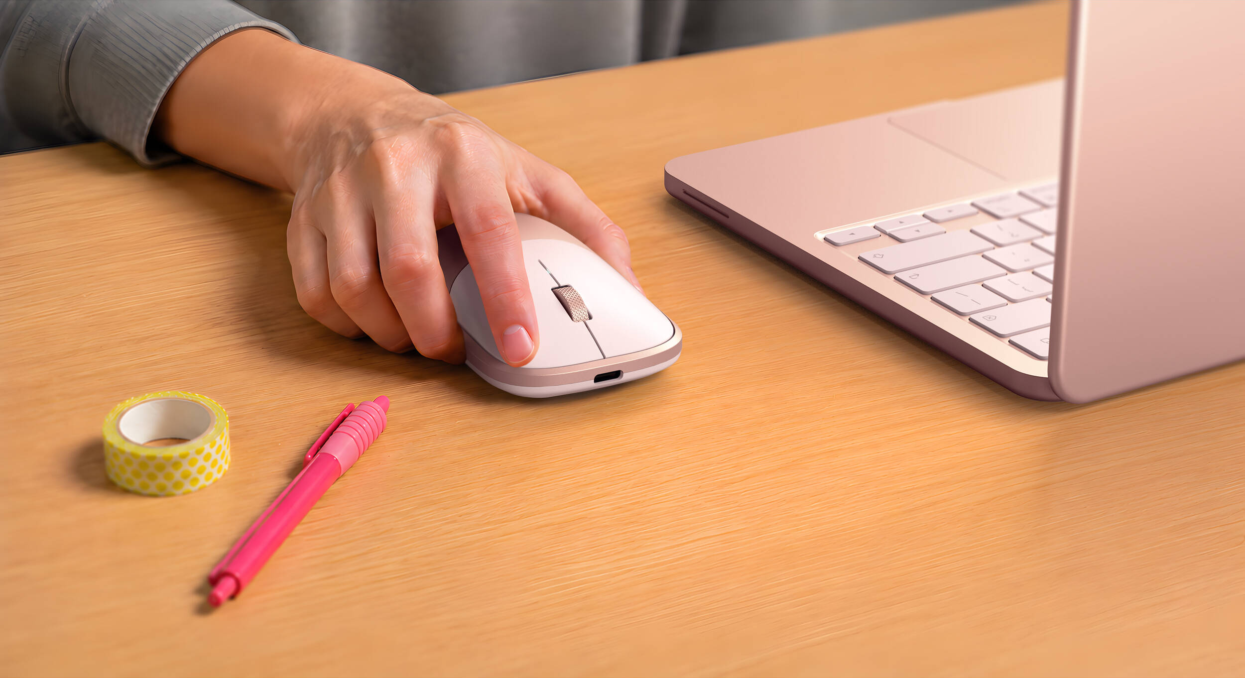 Une main utilise une souris blanche à côté d'un ordinateur portable or rose sur un bureau.