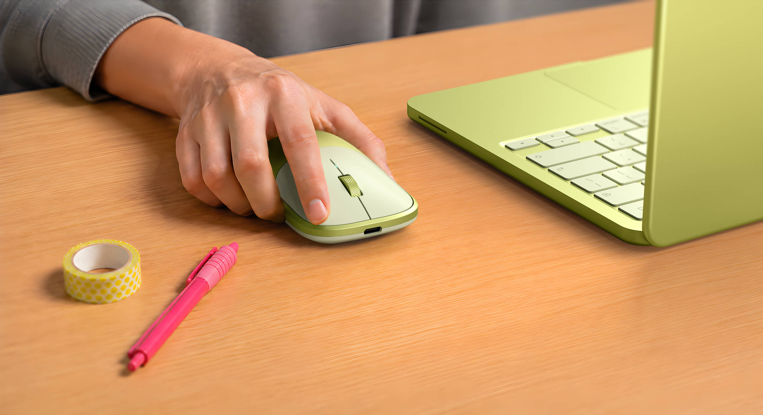 Une main utilise une souris à côté d'un ordinateur portable. Un stylo et du ruban adhésif sont à proximité.