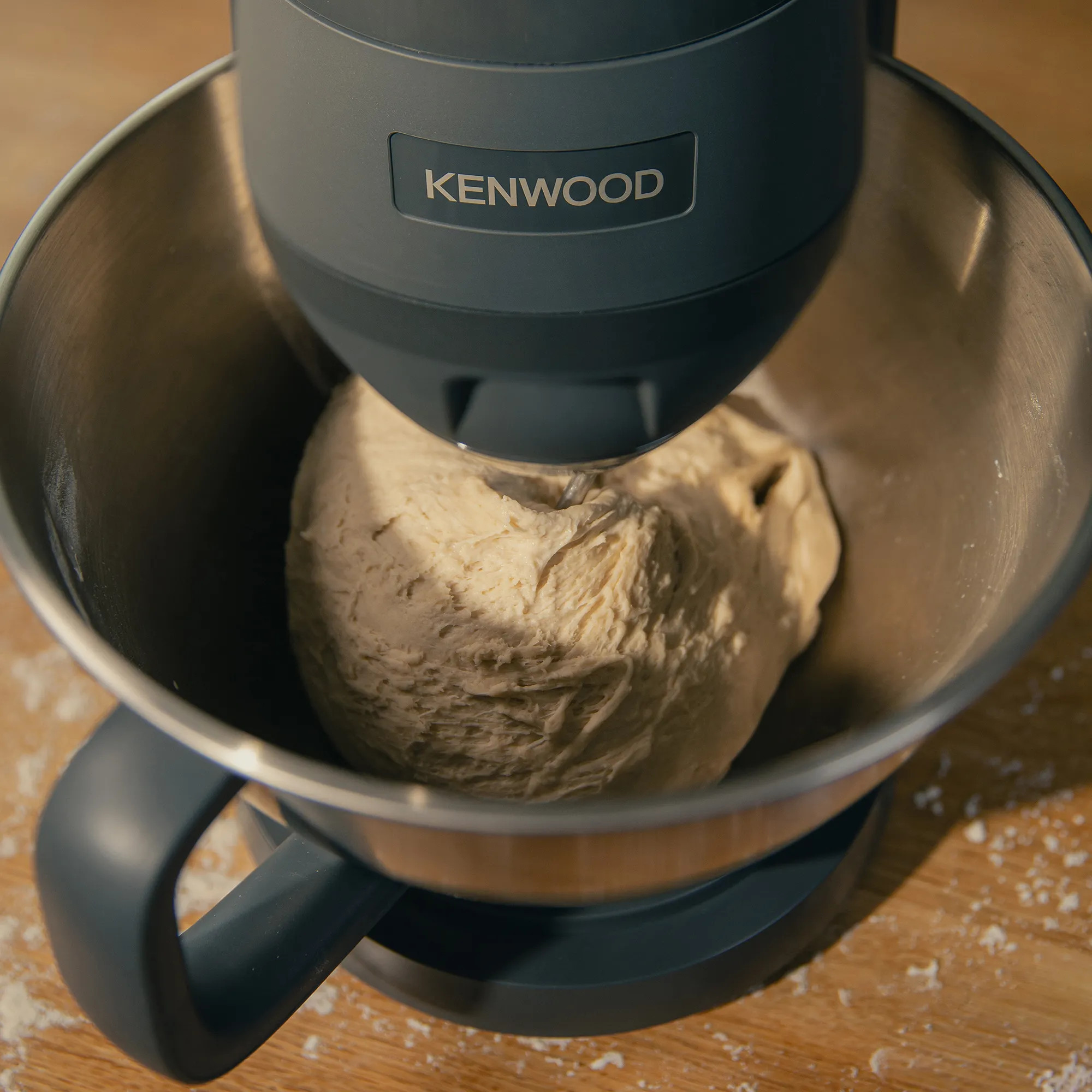 Robot kuchenny Kenwood zagniata ciasto w misie ze stali nierdzewnej na drewnianym stole.