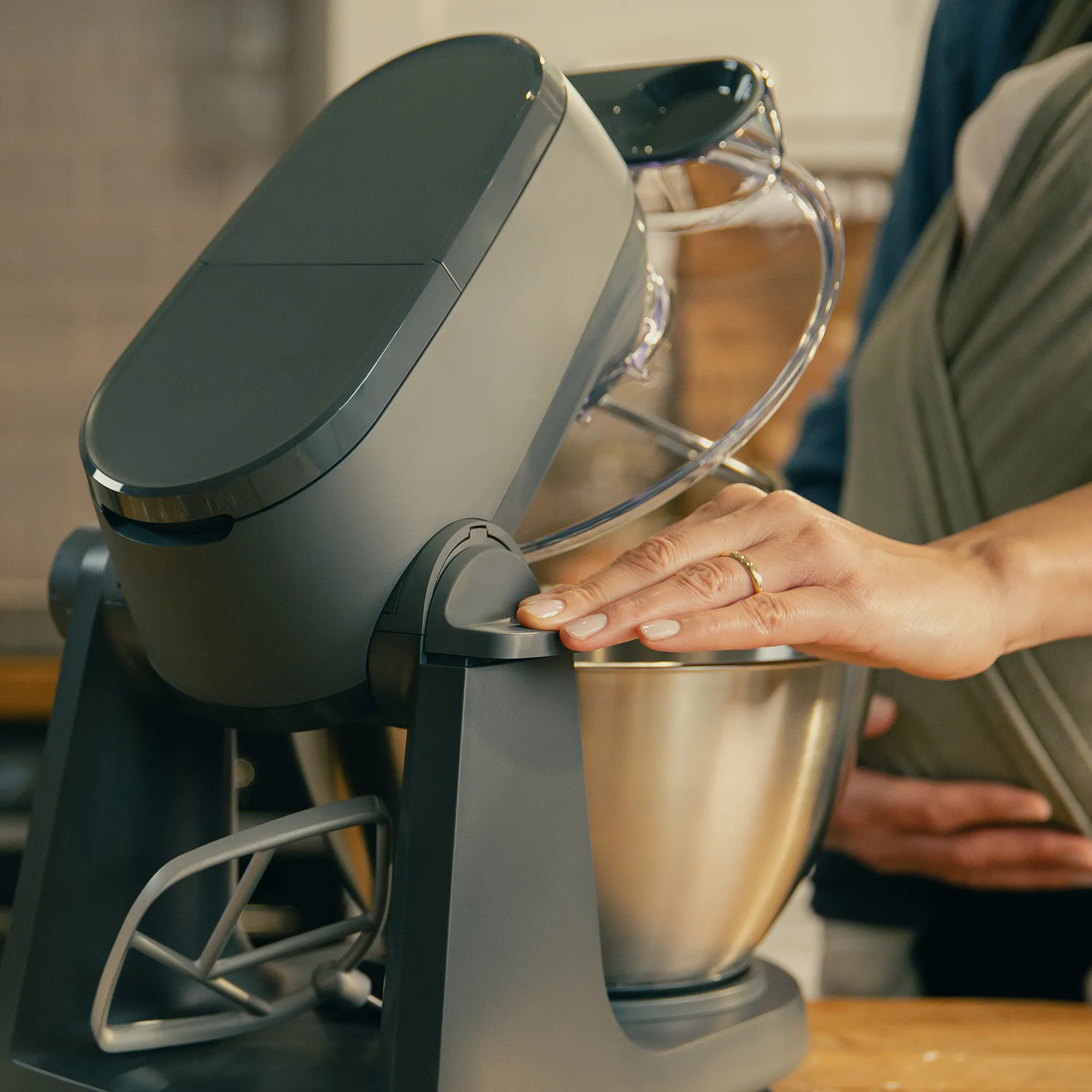Ręka obsługuje ciemny robot kuchenny ze stalową misą.