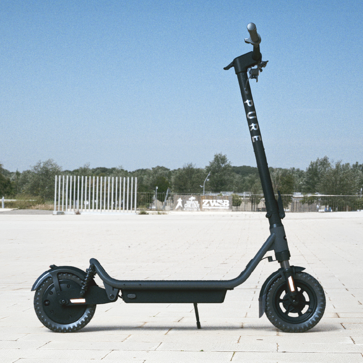 Ein schwarzer E-Scooter steht auf einem gepflasterten Platz vor Bäumen und blauem Himmel.