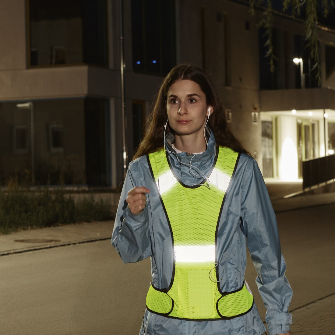 Eine Frau in reflektierender Weste joggt nachts auf der Straße.