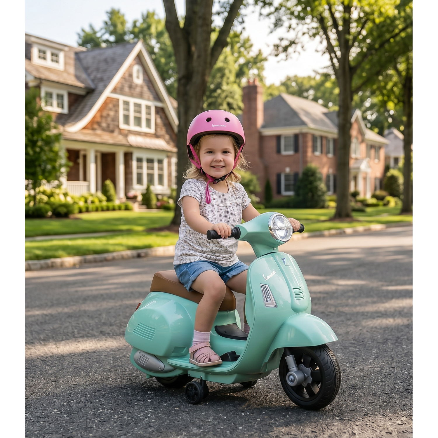 A smiling girl in a pink helmet rides a teal toy Vespa scooter on a suburban street.