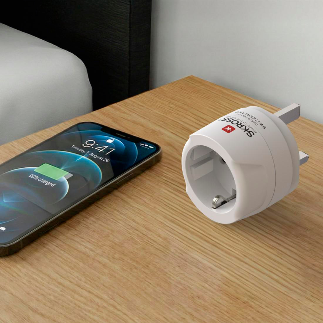 Ein Smartphone wird auf einem Nachttisch geladen, daneben ein Reiseadapter.