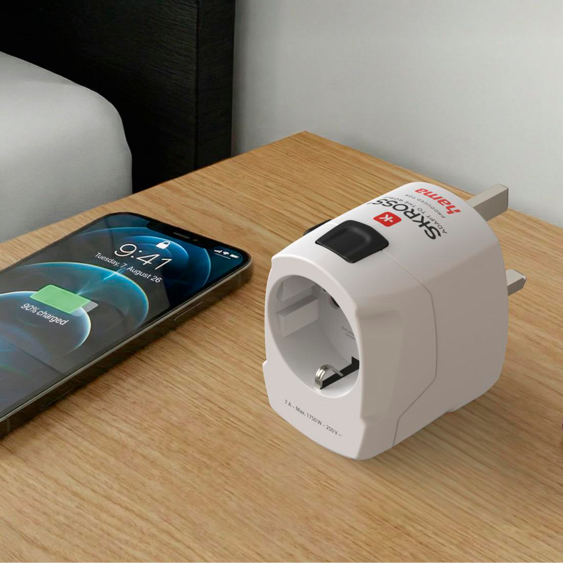 Ein weißer Reiseadapter und ein Smartphone mit 90% geladenem Akku auf einem Nachttisch.