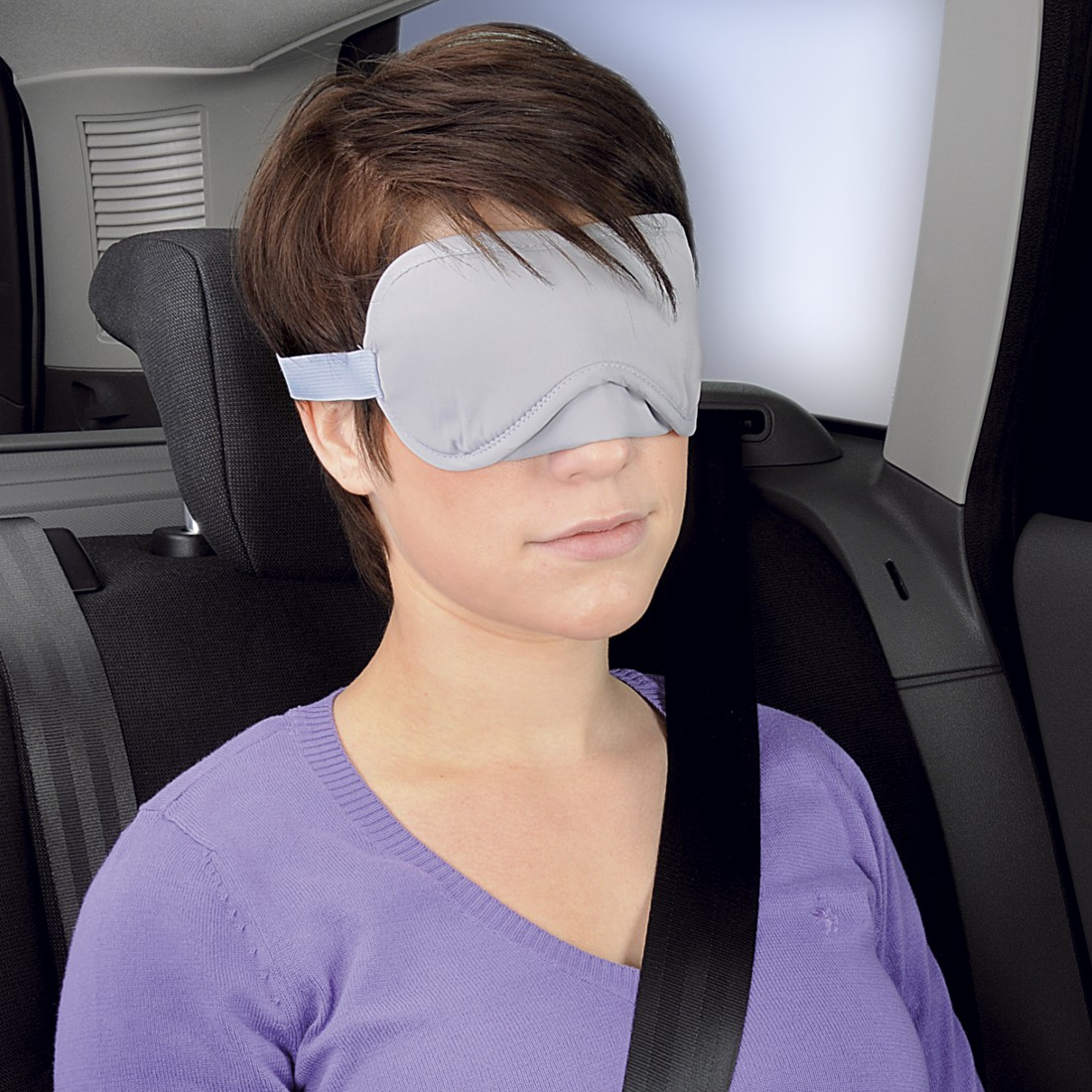 Frau mit Schlafmaske im Auto, trägt lila Pullover und Sicherheitsgurt.