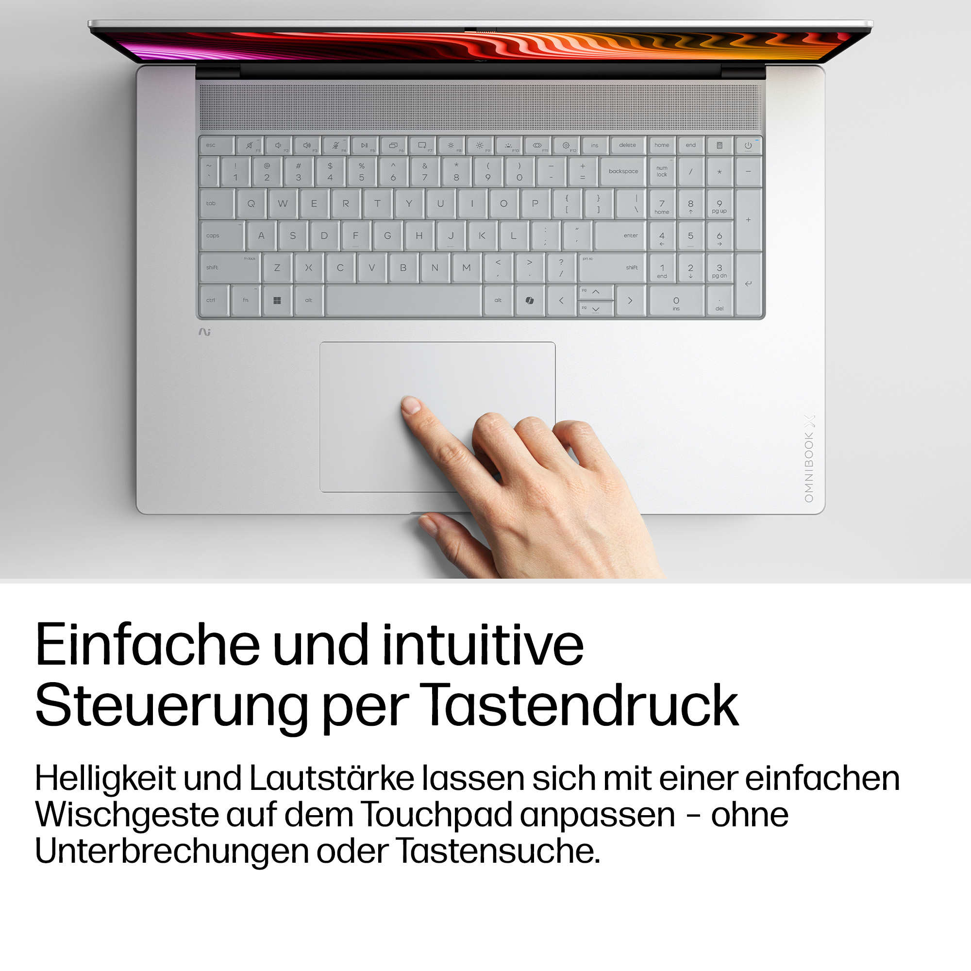 Eine Hand bedient das Touchpad eines hellgrauen Laptops mit beleuchteter Tastatur.