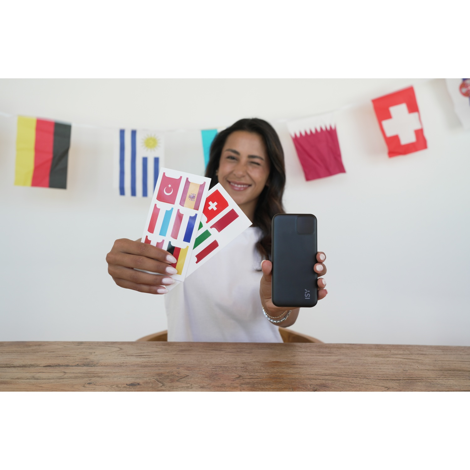 Donna tiene telefono e cartoline di bandiere davanti a ghirlanda di bandiere. Tavolo in primo piano.