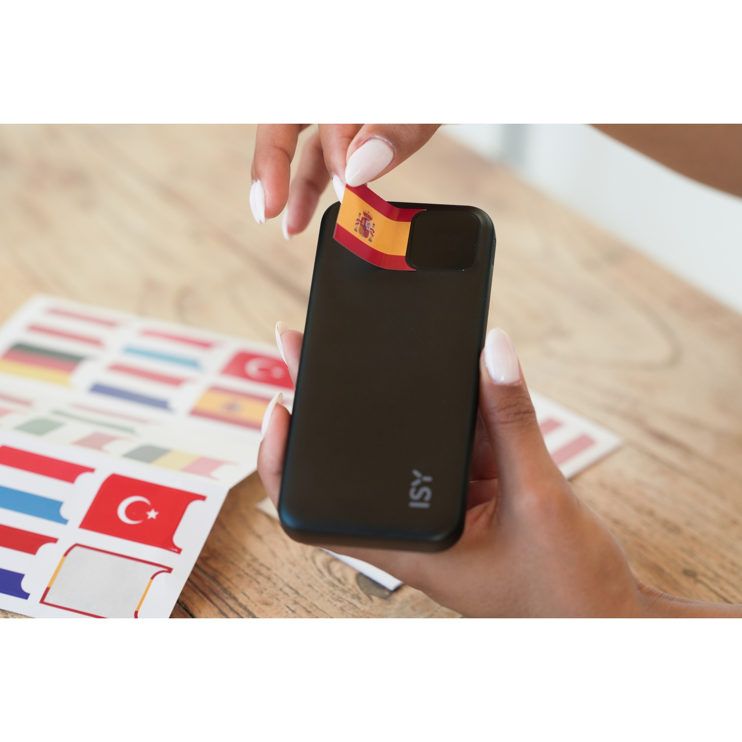 Mani che applicano un adesivo bandiera spagnola a un telefono nero, vicino ad adesivi.