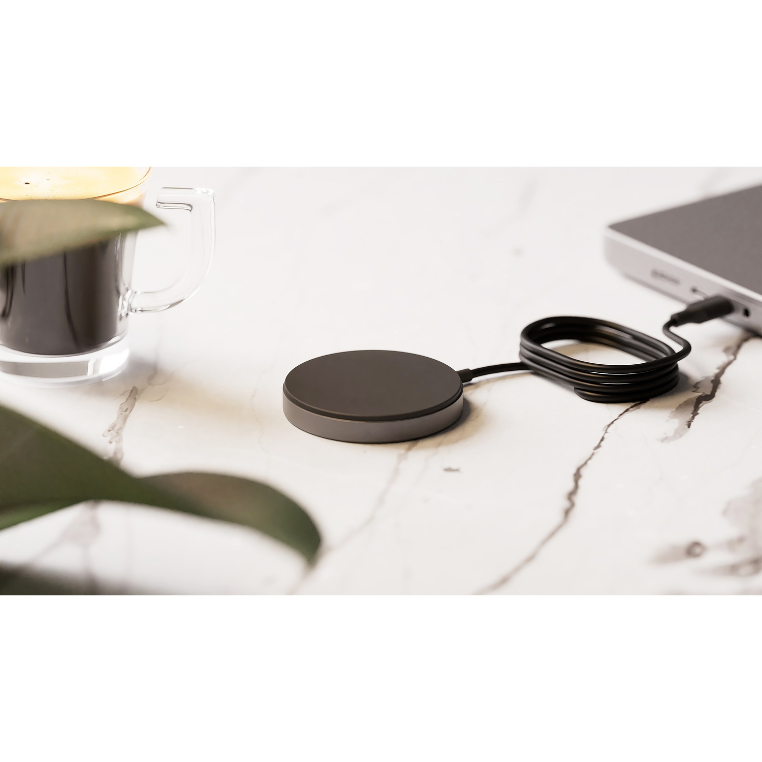A black charging puck with cable and a silver device on marble.