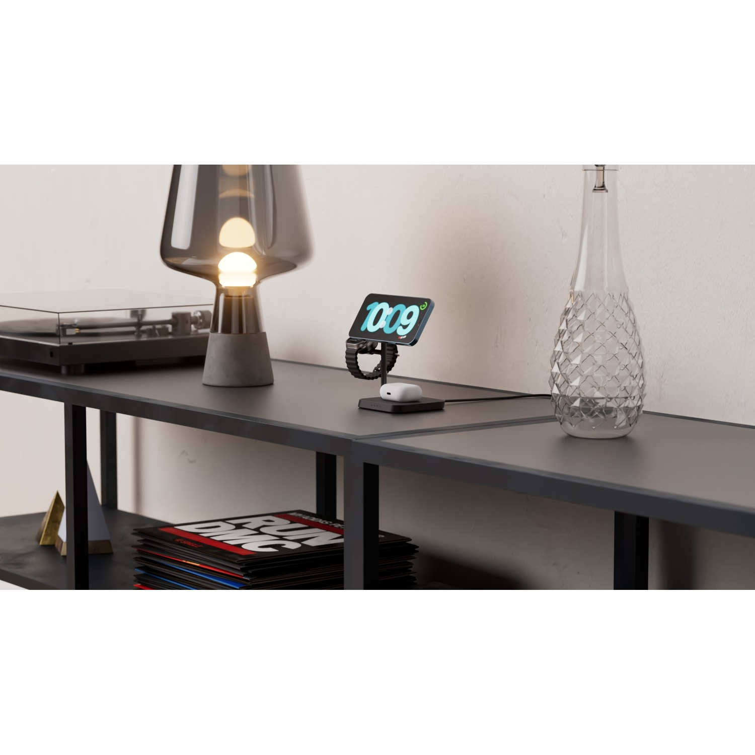 A black shelf with a turntable, a dark gray lamp, a phone and smartwatch on a charger, and a glass decanter.