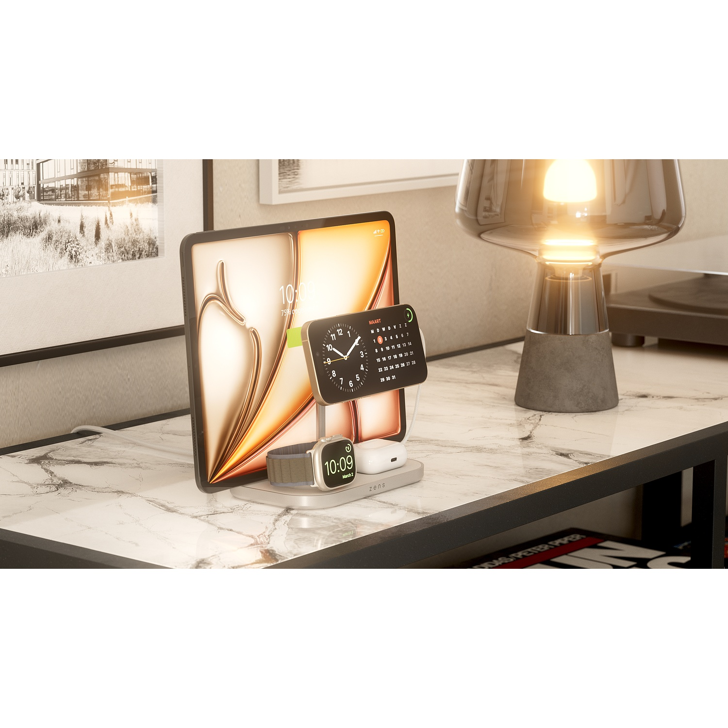 A tablet, smartphone, smartwatch, and earbuds charging on a gray stand on a white marble table with a lamp.