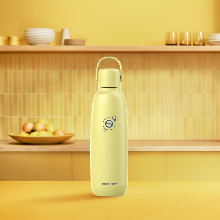 Jasnożółta butelka Sodastream stoi na żółtej powierzchni w kuchni.