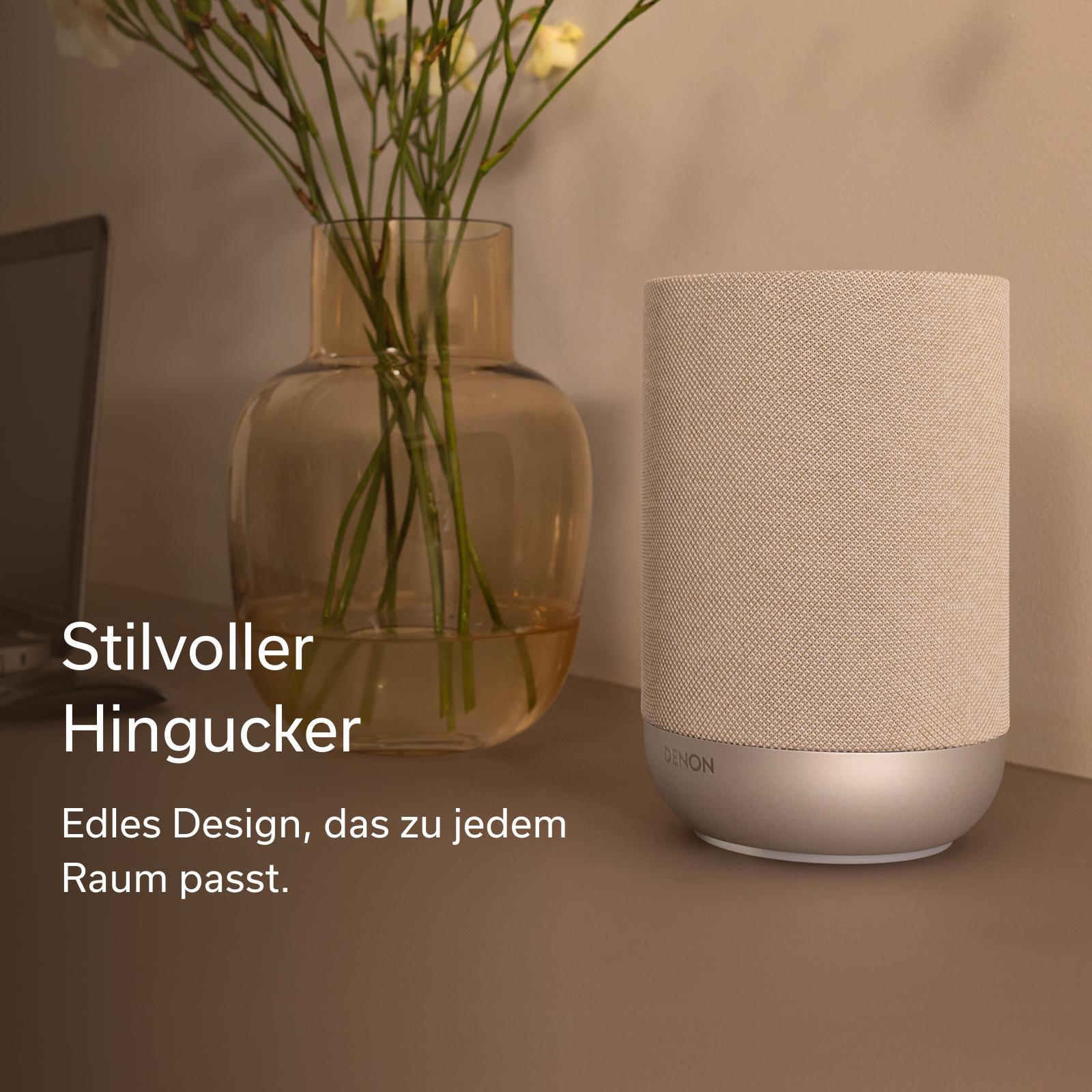 Ein heller Lautsprecher neben einer Vase mit Blumen und einem Laptop.